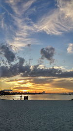 Silhouette people on beach against sky during sunset