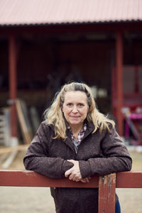 Portrait of female farmer leaning on fence
