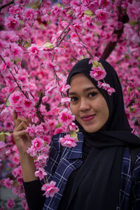 Portrait of woman with pink flower standing against trees