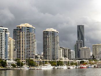 Modern buildings by river against sky in city