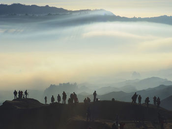 Silhouette people standing on mountain peak during foggy weather