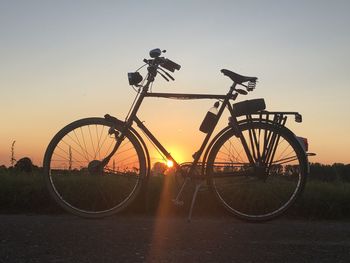 Bicycle on field against clear sky during sunset