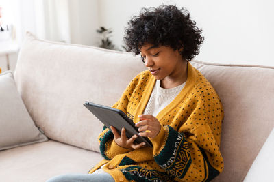 Young woman using mobile phone while sitting on sofa at home