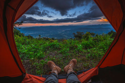 Low section of man lying in tent against sky during sunset