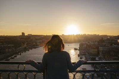 Rear view of woman standing by railing against river and buildings