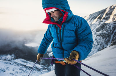 Male climber belays his lead climber during a cold winter alpine climb