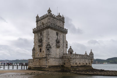 View of building by river against cloudy sky