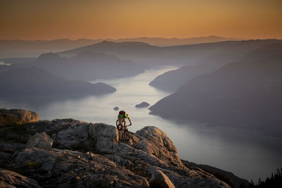 Full length of man cycling on rock against mountain range