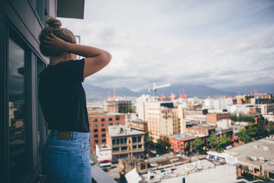 Rear view of woman standing against sky in city