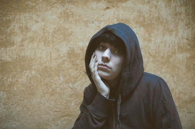 Portrait of sad woman in hooded shirt against wall