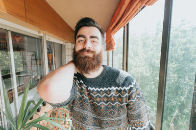 Portrait of young man standing against window