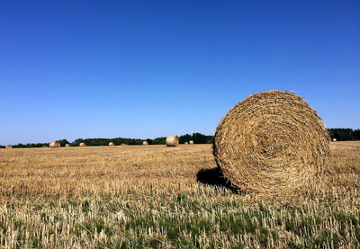 Hay bales on field against clear blue sky during sunny day