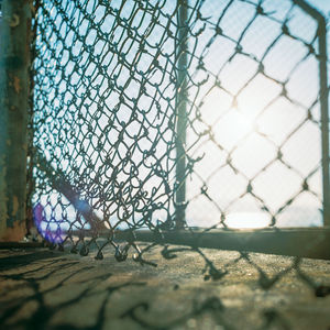 Close-up of chainlink fence against sky on sunny day