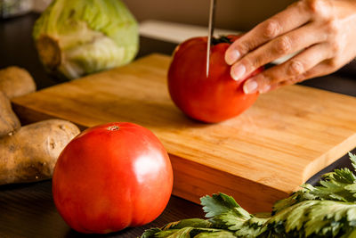 Cropped hand of man holding tomatoes on cutting board