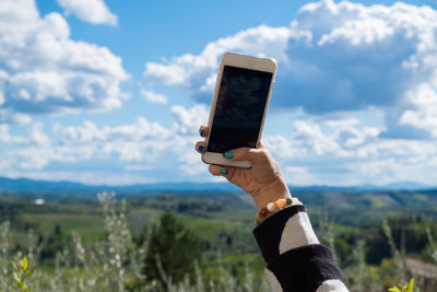 Cropped hand photographing cloudy sky using smart phone