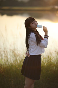 Side view of young woman standing against trees