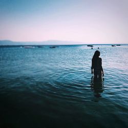 Rear view of teenage girl in sea during sunset