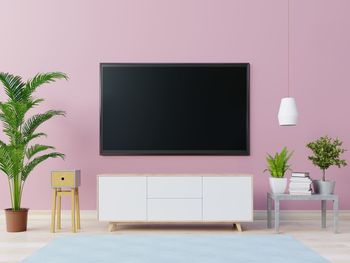 Television set over cabinet against pink wall at home