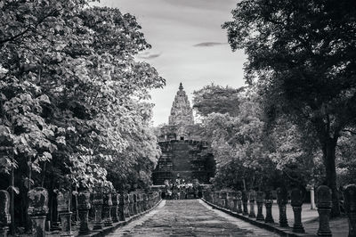 Walkway amidst trees and buildings against sky