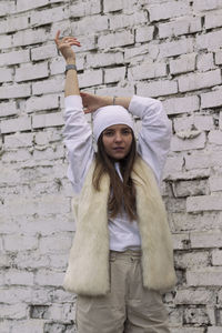 Portrait of young woman standing against brick wall