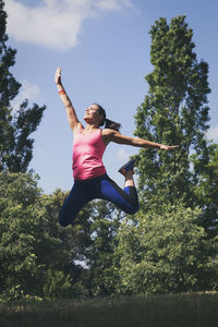 Low angle view of woman jumping against trees