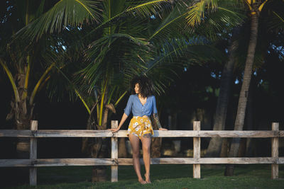 Full length of woman standing on field against fence and trees