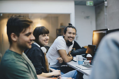 Happy male and female computer programmers talking at desk in office