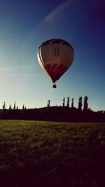 Hot air balloon flying over field against clear sky