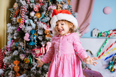 Funny child little girl in santa claus hat and pink dress laughs with happiness