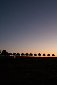 Silhouette trees on field against clear sky