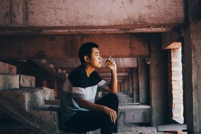 Side view of young man smoking while sitting at abandoned