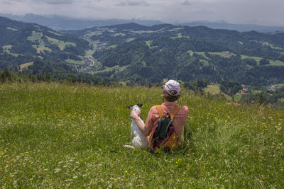 Man with dog sitting on mountain against sky