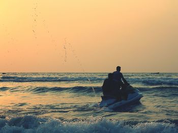 People riding jet boat in sea against sky during sunset