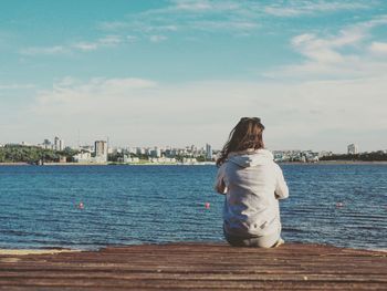 Rear view of woman standing on retaining wall by sea against sky