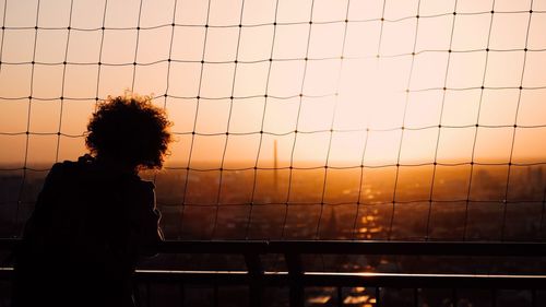 Silhouette woman standing by railing with net against sky during sunset