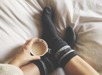 Low section of person holding coffee cup on bed