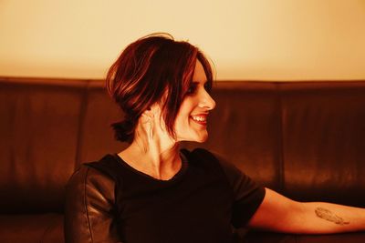 Close-up of woman smiling while sitting against sofa