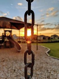 Close-up of metal chain on field against sky during sunset