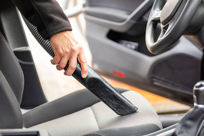 Cropped hand of man using vacuum cleaner in car