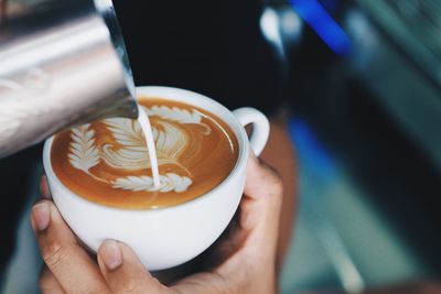Close-up of hands pouring milk in coffee