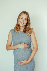 Portrait of smiling pregnant young woman standing against white background