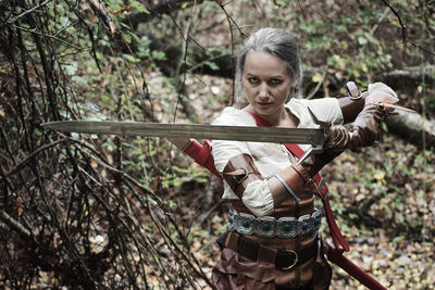 Portrait of young woman wearing costume holding sword at forest