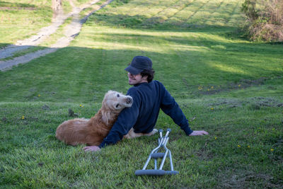 Loving old golden retriever dog rests on a grassy hill with a young man by crutches on the ground
