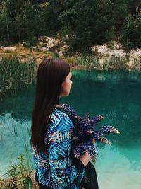 Rear view of woman standing by lake against trees