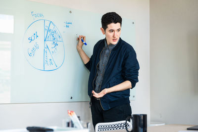 Confident young businessman discussing over diagram in board room at office