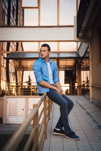 Young man looking away while sitting on railing