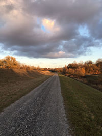 Road amidst field against sky during sunset