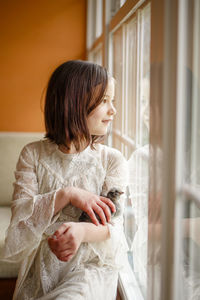 A small happy girl reflected in window holds a baby chick in her hands