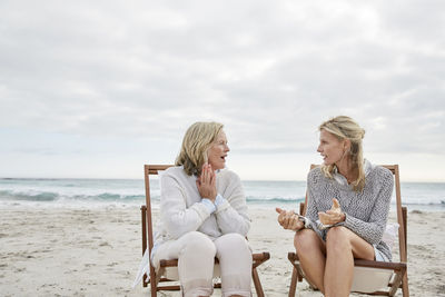 Mother and daughter talking on the beach sitting in deck chairs