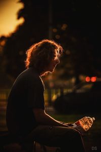 Side view of person sitting on illuminated city at night